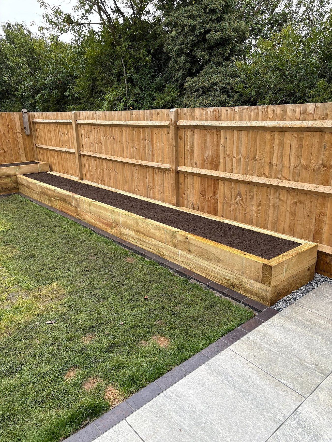 Pressure-treated sleeper raised bed mid-build, with rebated joinery, capped tops, charcoal block edging and porcelain terrace foreground &mdash; Warsash 2025