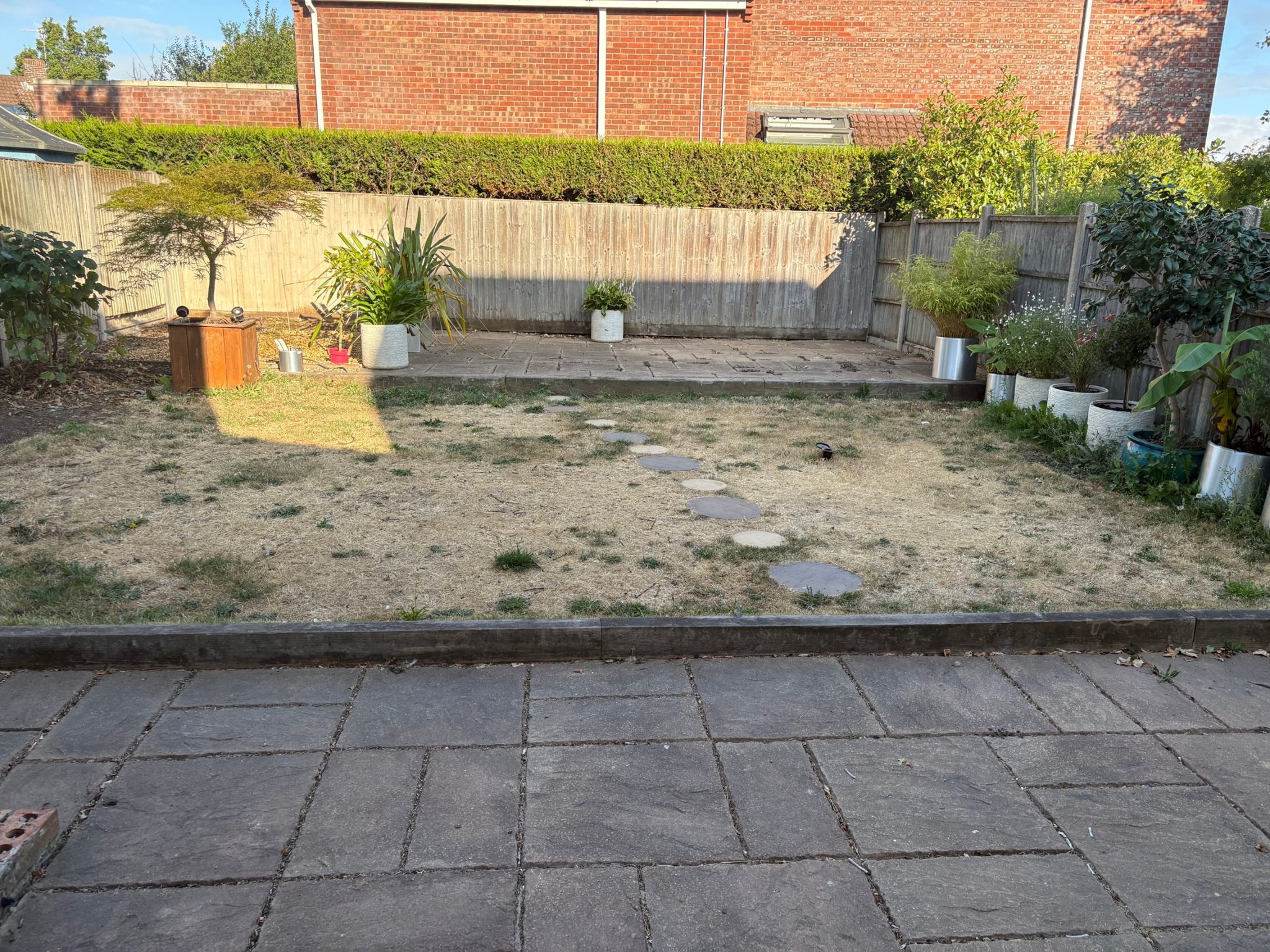 Before: riven-effect slabs at the house, an old sleeper edge, a dried-out lawn with stepping stones and a slab patio against the back fence.
