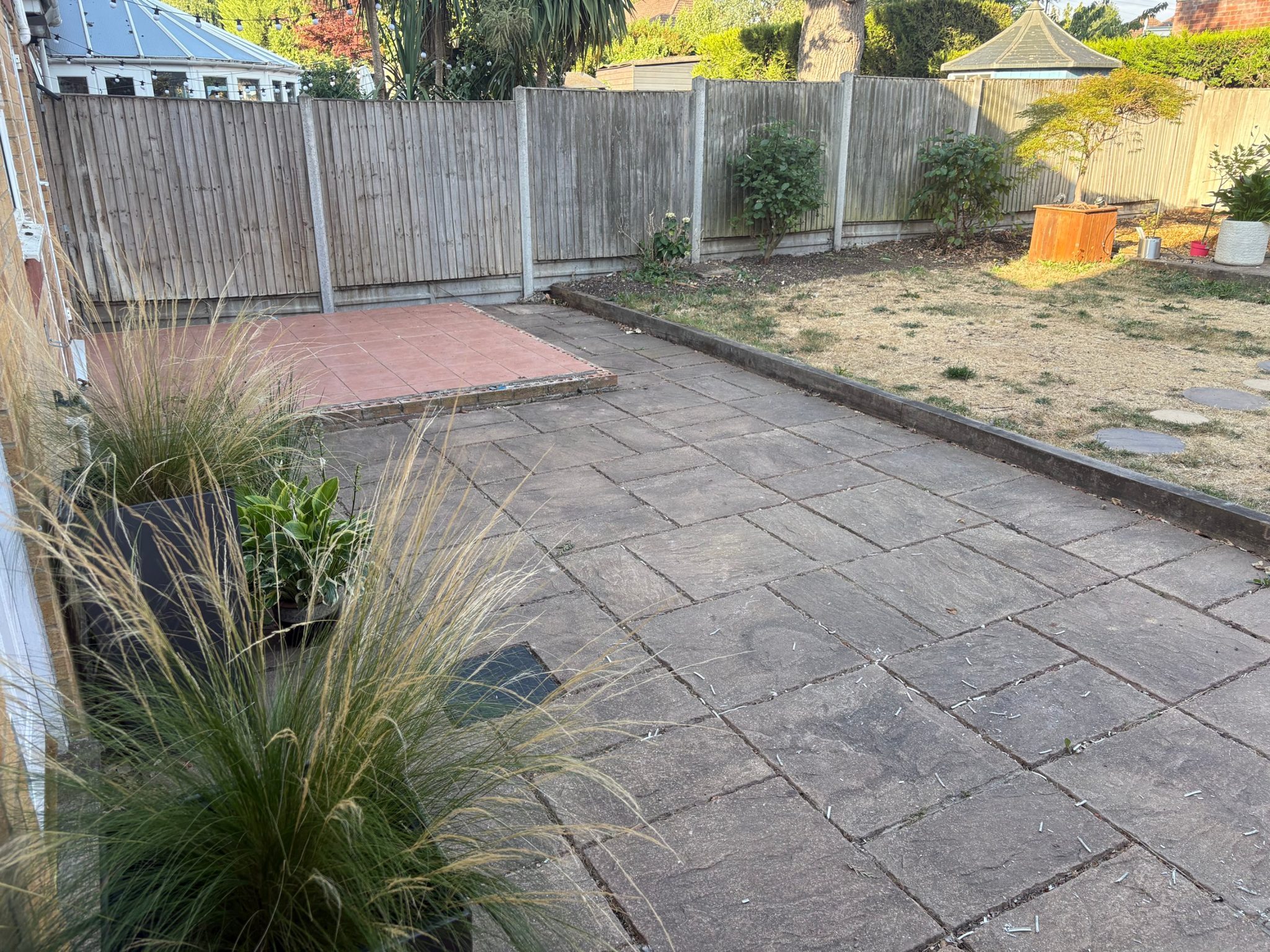 Before: the old slab patio along the house with the tired lawn and fence line beyond.