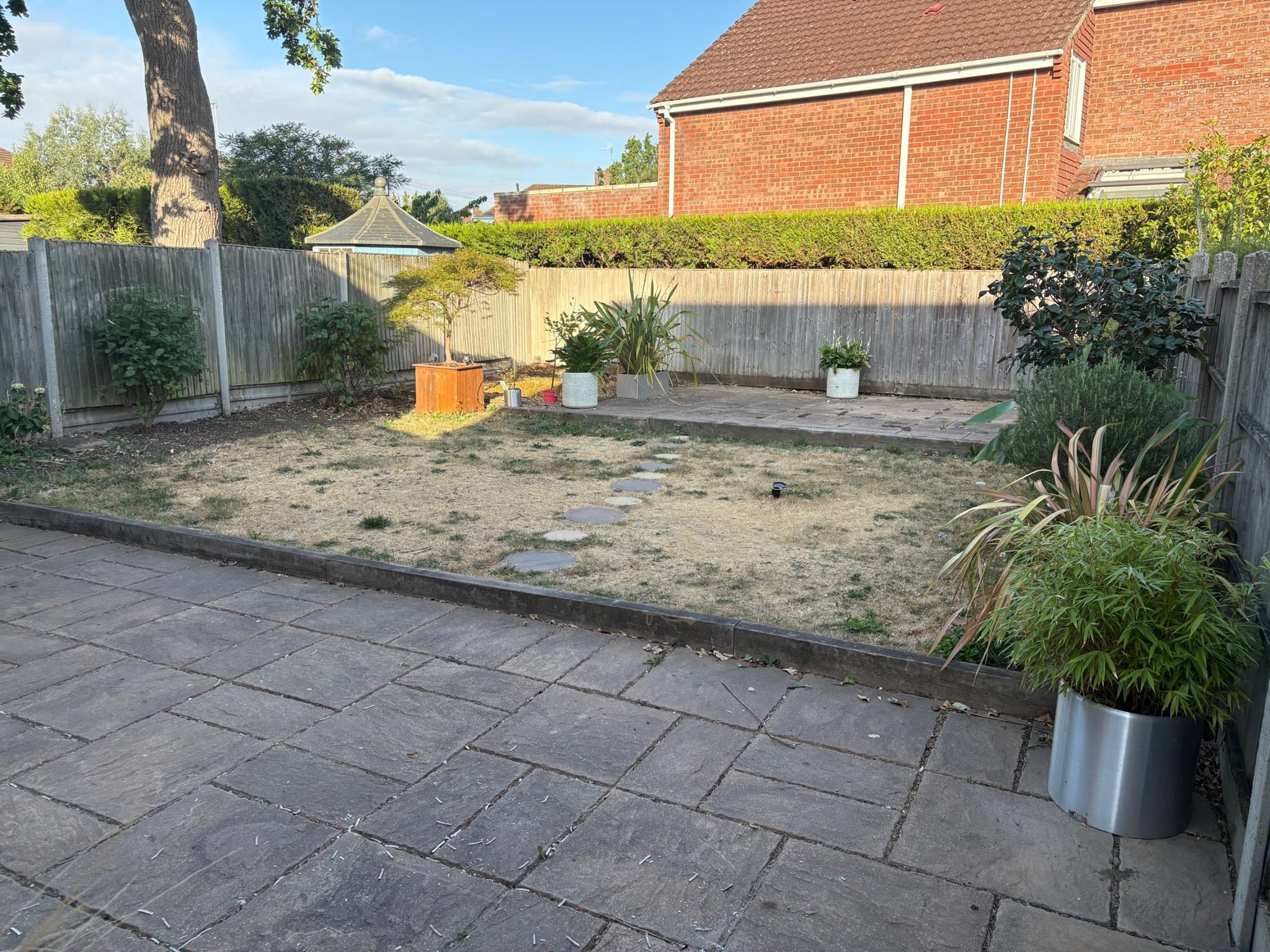 Before: wide view of the lower patio, sleeper edge, stepping stones and the slab patio at the back of the garden.
