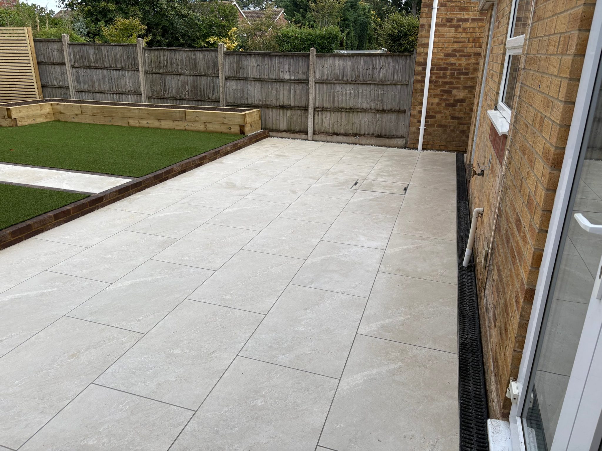 The lower porcelain terrace along the back of the house, with a black linear drain channel running the length of the wall.