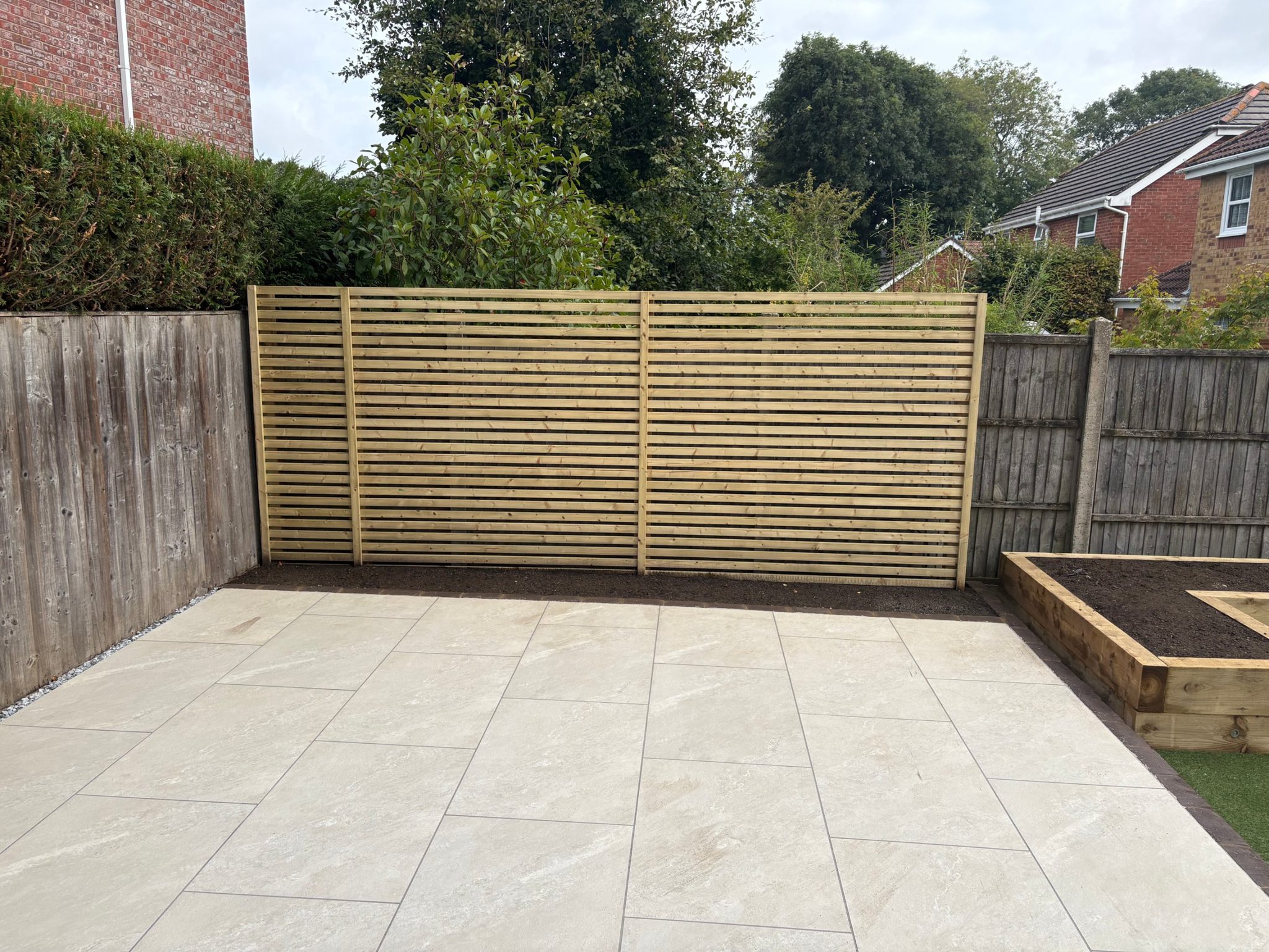 The Venetian-style slatted screen on the right-hand side of the upper patio, with a fresh planting bed along its base.