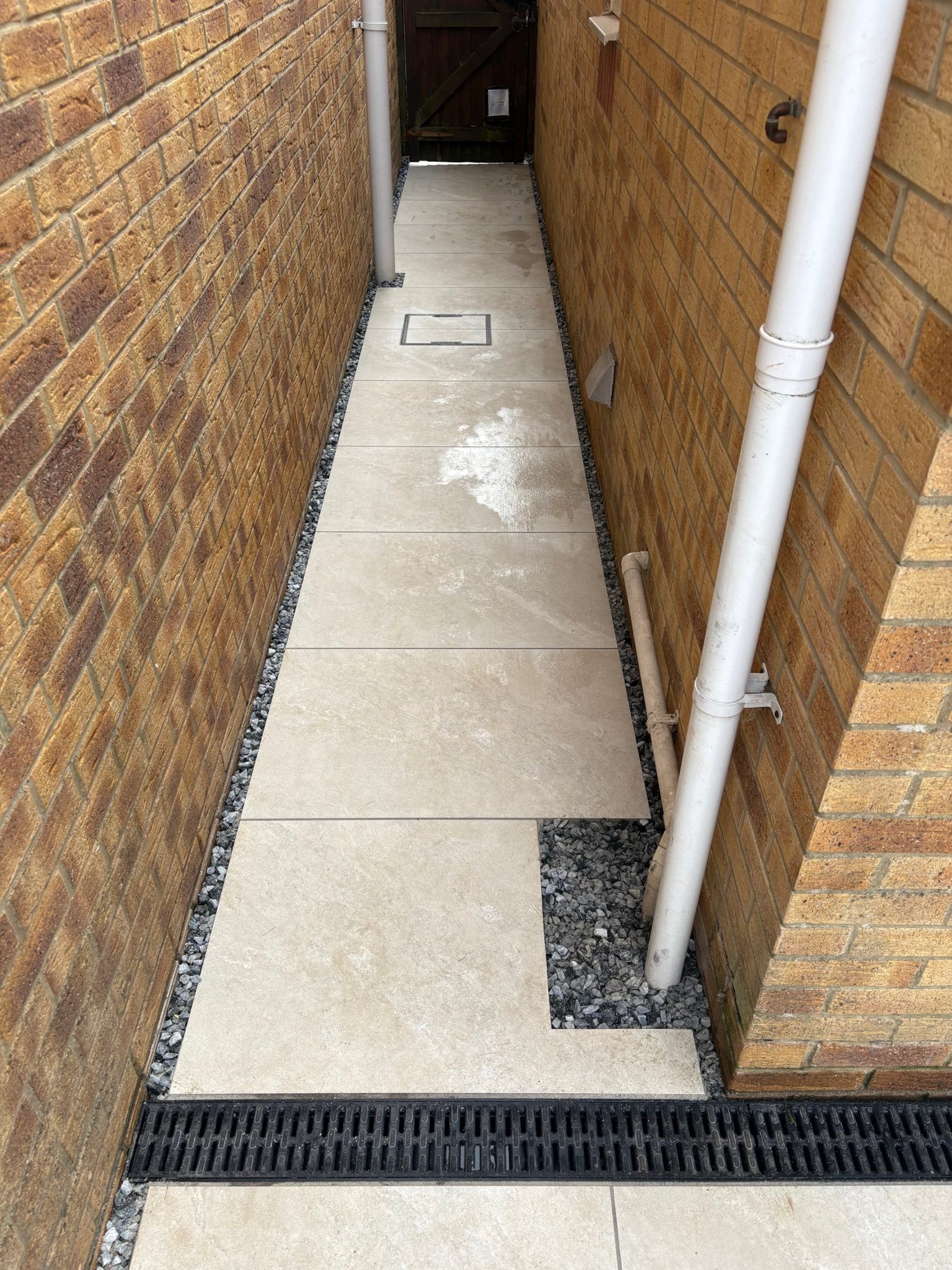 After: the side return relaid in matching porcelain, a recessed access cover, grey chippings margins and a linear drain where it meets the terrace.