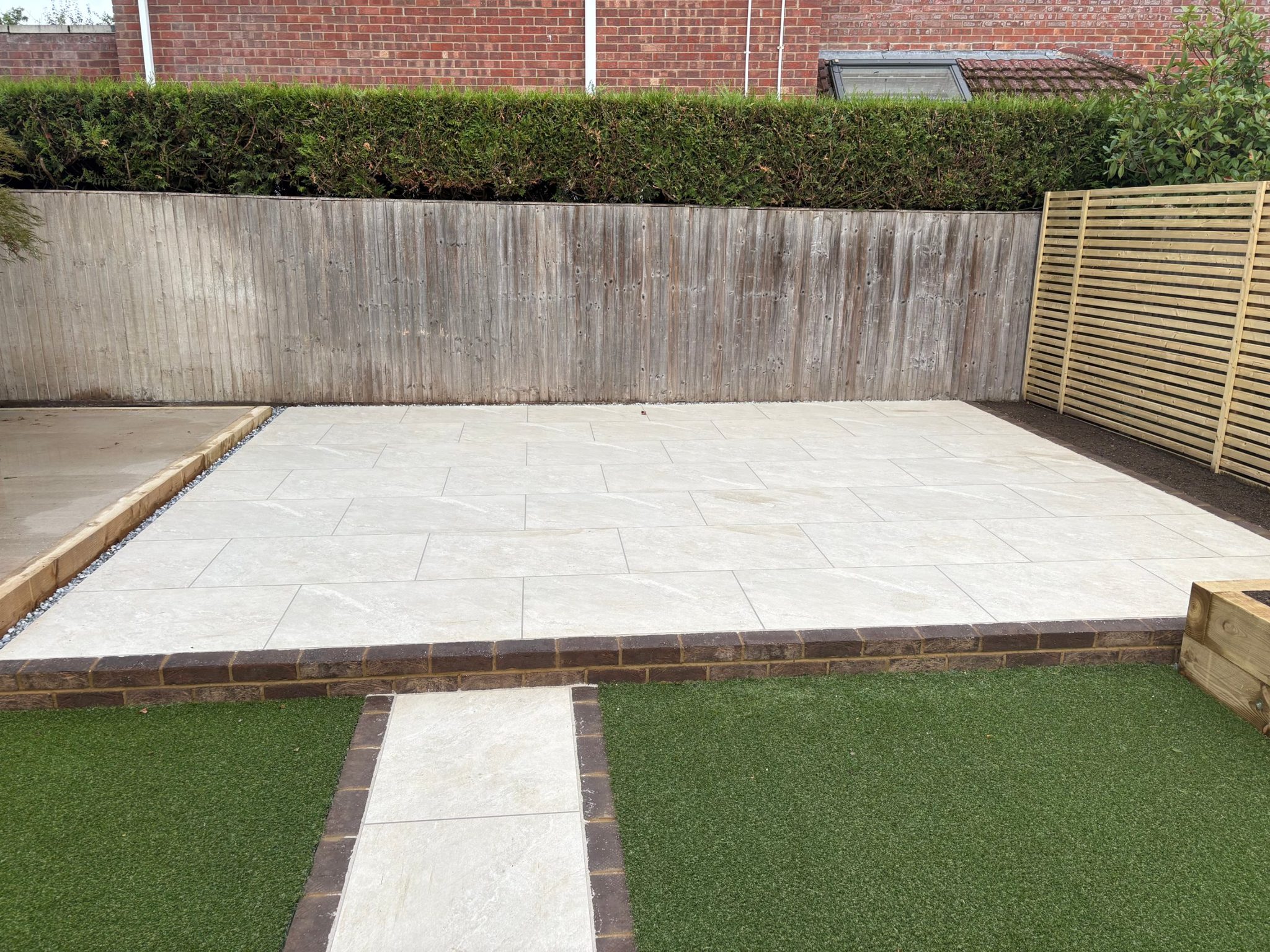 The upper patio in Himalayan White porcelain, its dark brick edge doubling as the step down to the porcelain path.