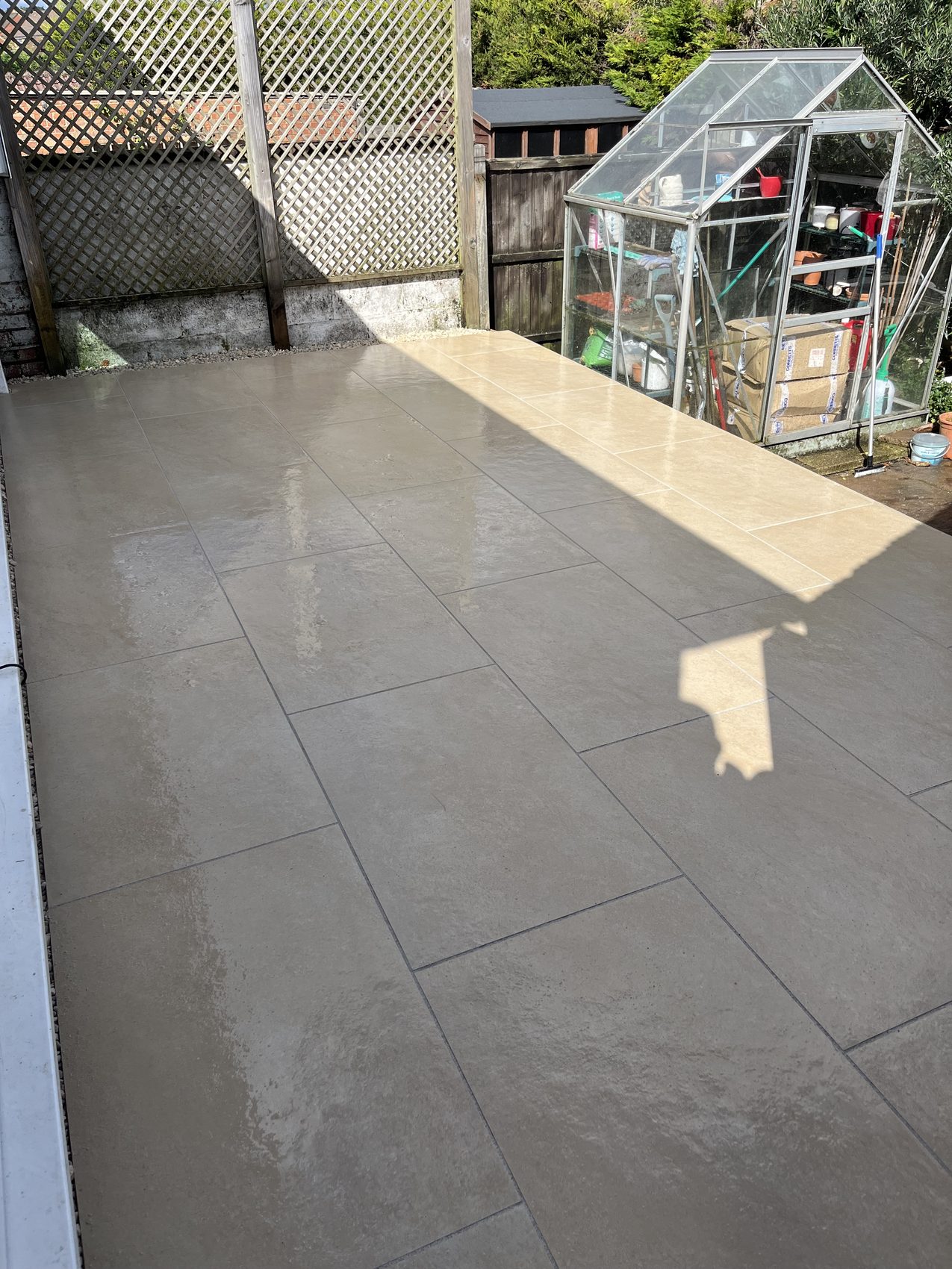 The finished porcelain patio catching the afternoon sun, greenhouse beyond.