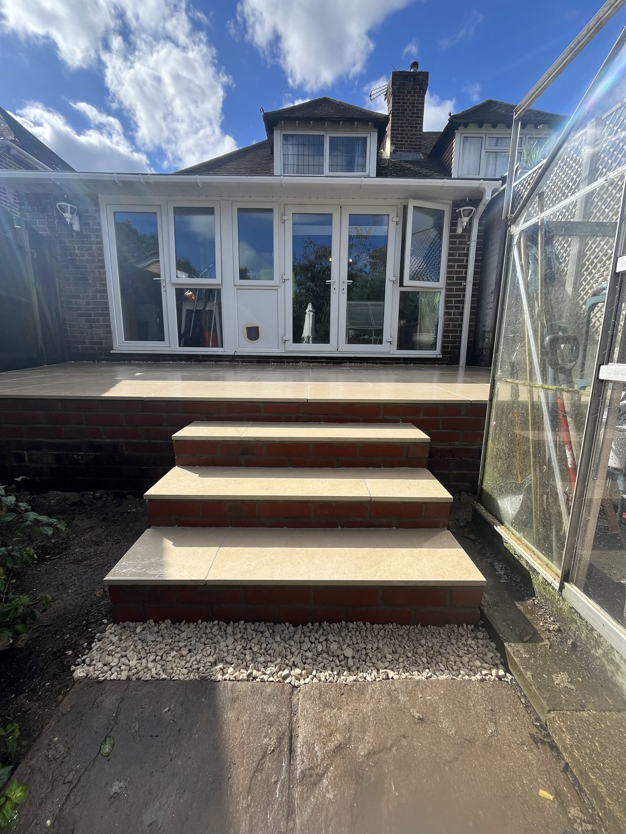 The finished Fareham garden: a raised beige porcelain patio with matching brick-faced steps down to the lower garden, replacing the old timber decking, 2026