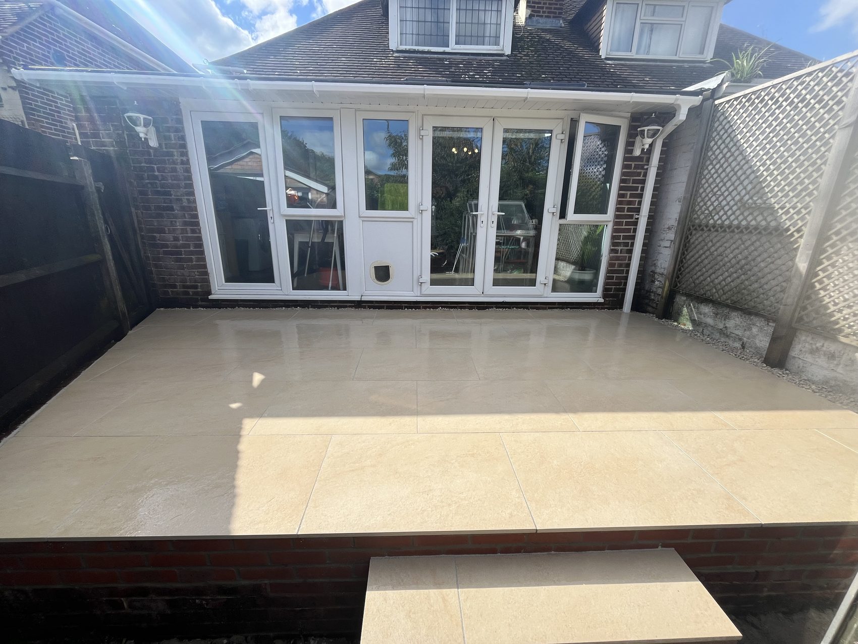 The new beige porcelain patio running the full width of the house, steps down to the lower garden just visible.