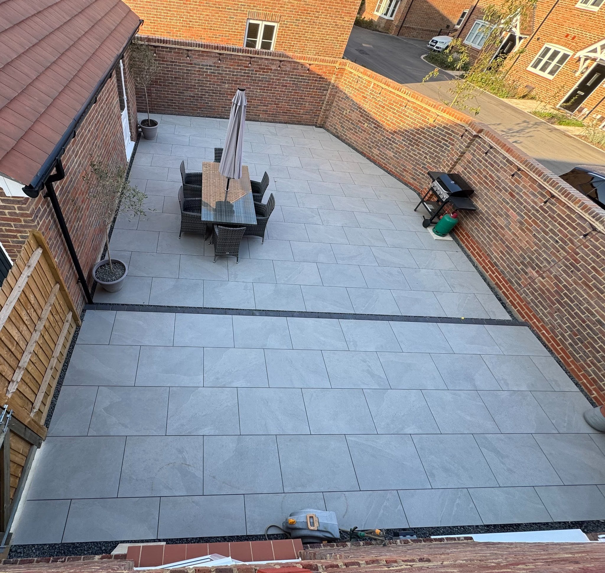 Two-tier porcelain patio for a new-build Fareham property — Victoria Grey porcelain on both terraces, solid blue engineering brick step between the levels, Derbyshire Peak gravel channel, carbon pointing throughout