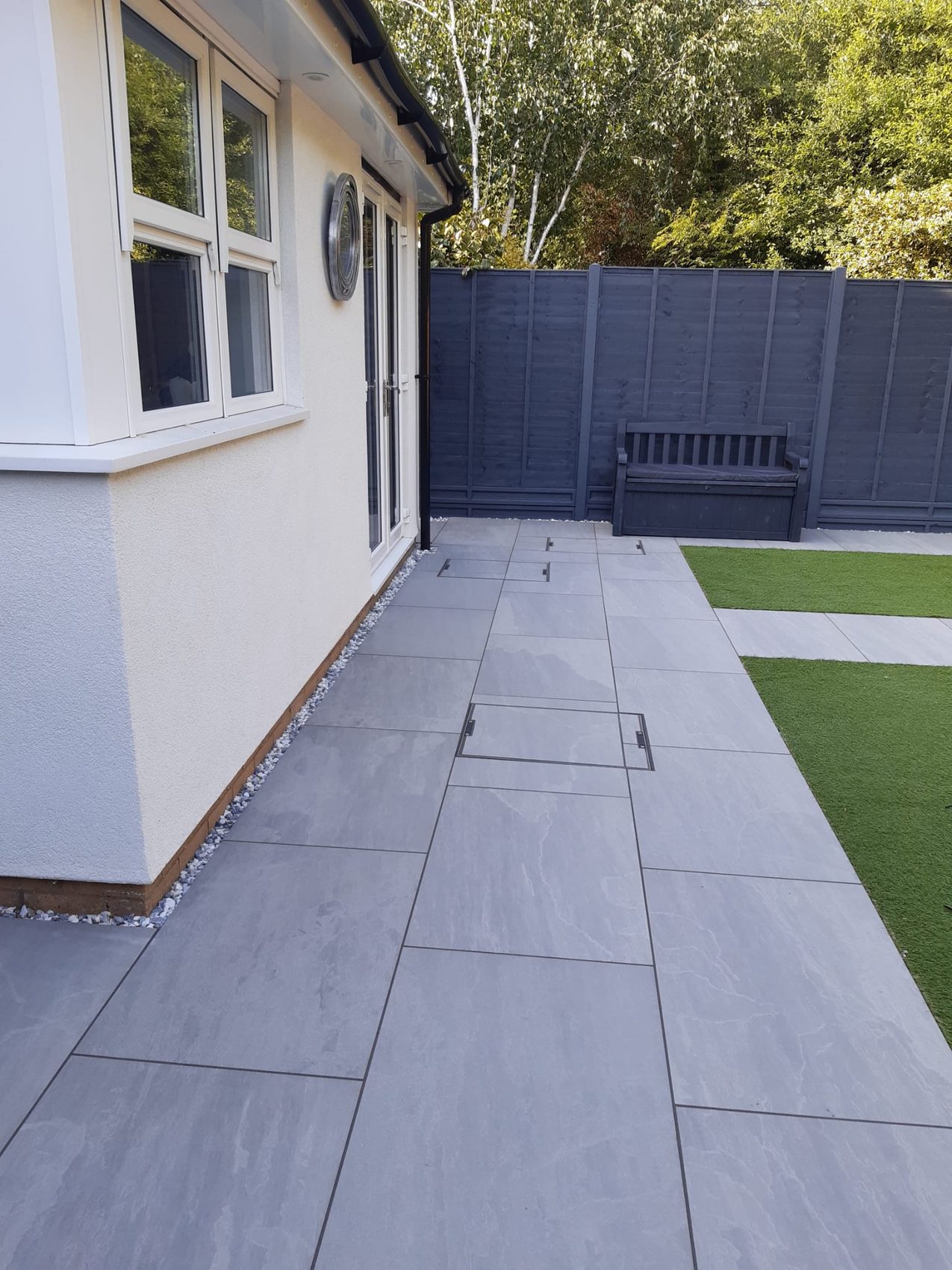 The new Kandla Grey porcelain patio, with inspection covers recessed and cut flush into the paving so they read as part of the surface, not a patch on it.