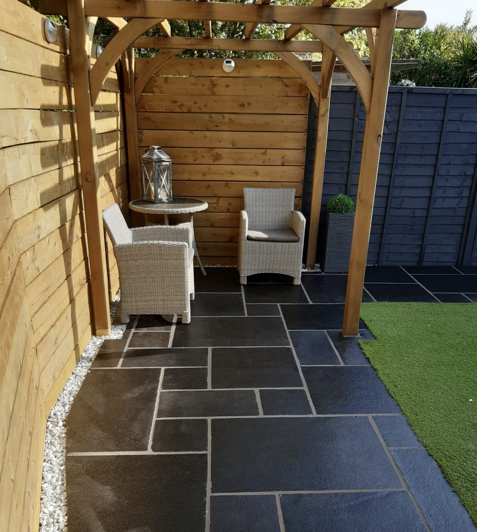 The existing black limestone paving, deep-cleaned and relaid true, now anchoring a seating area under the garden's pergola.