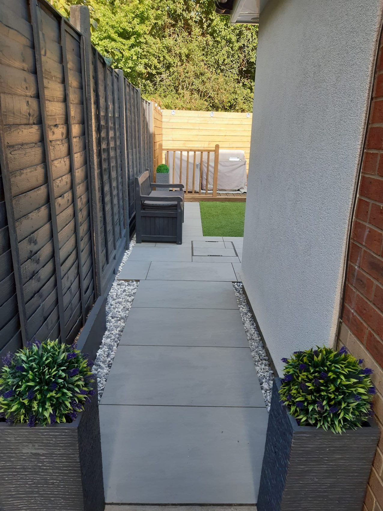 A porcelain side path edged in Polar Ice decorative stone, leading past clipped topiary to the black limestone patio beyond.