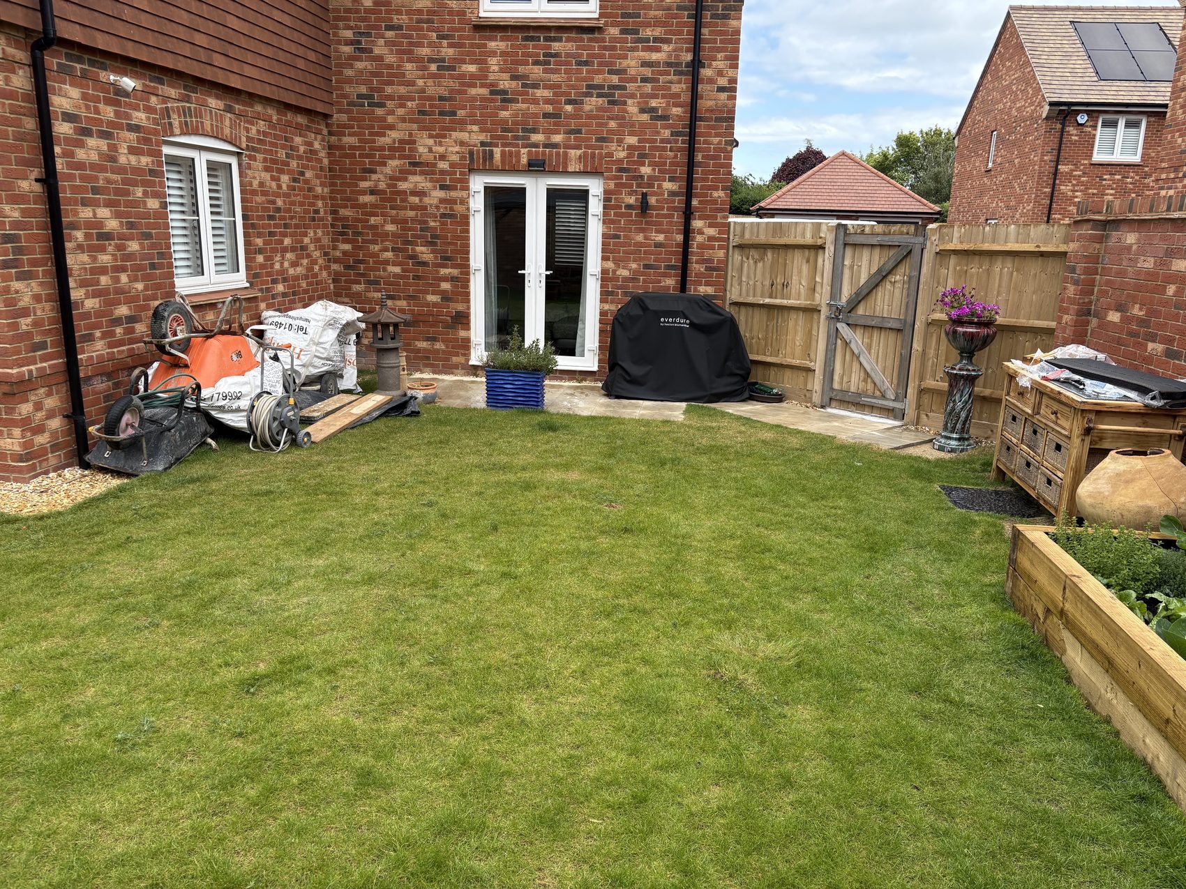 Before: garden tools, aggregate bags and a wheelbarrow crowding the only paved corner of the garden, next to a wooden side gate.