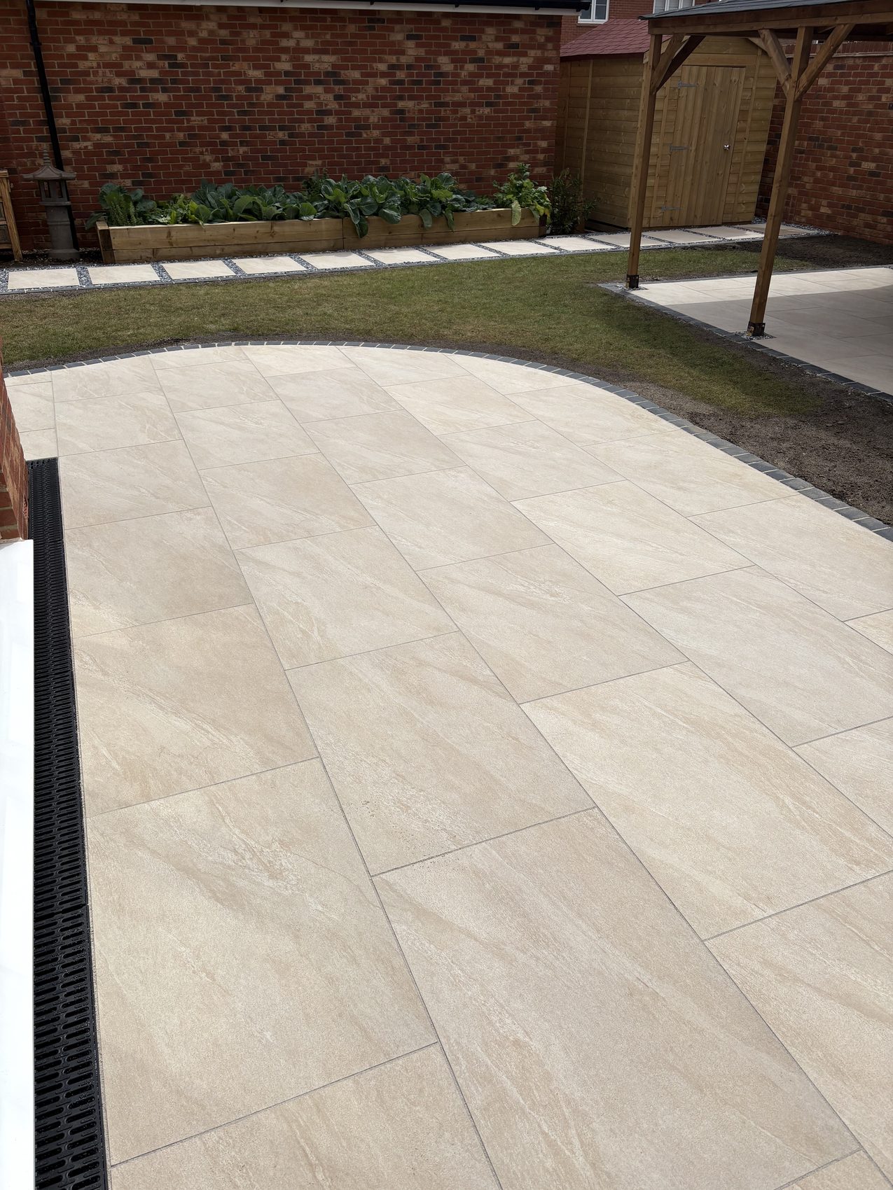 The curved edge of the new porcelain terrace, framed in black limestone setts against the lawn.