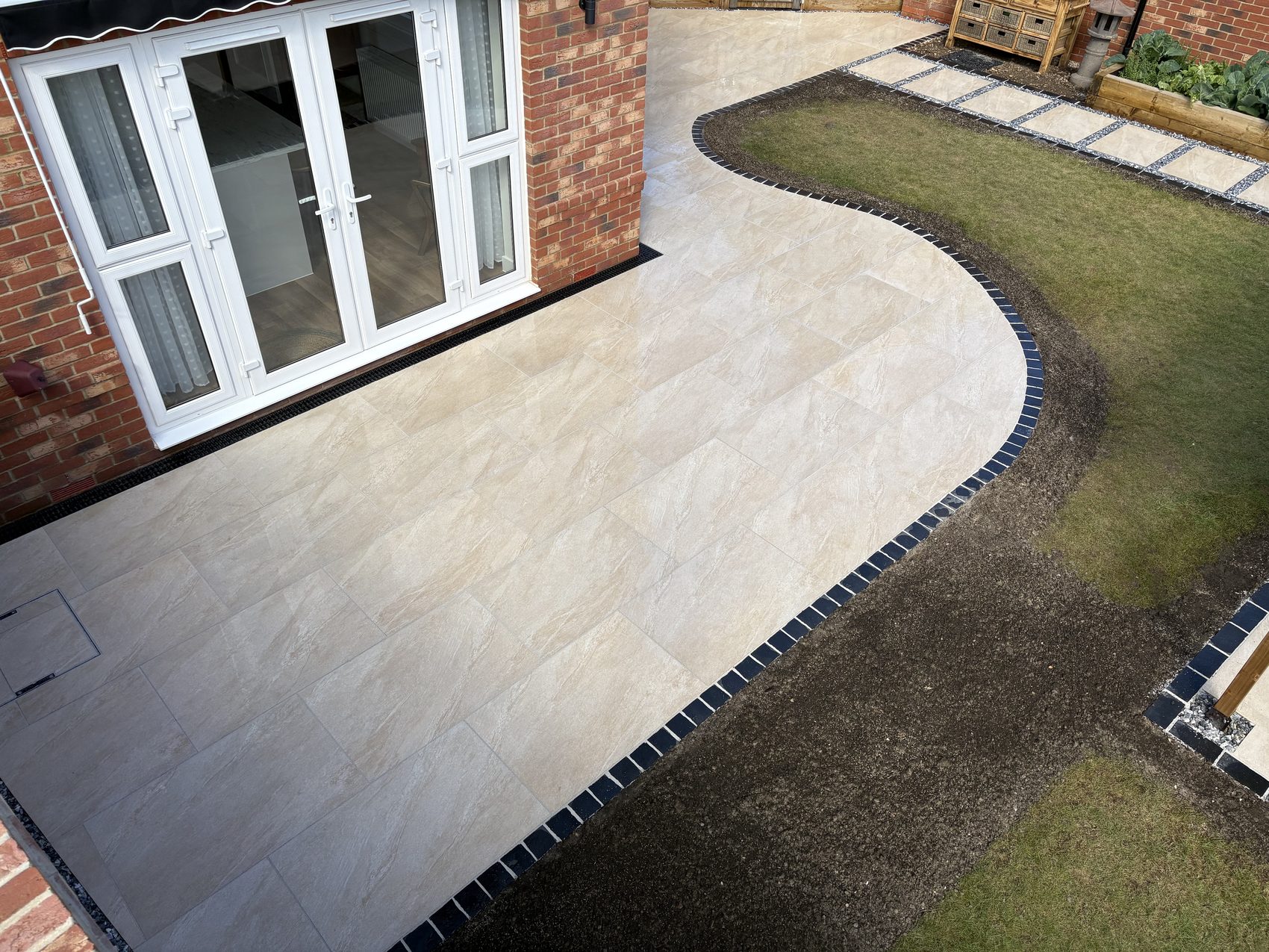 The curved terrace flowing from the back doors into the lawn, framed in black limestone.