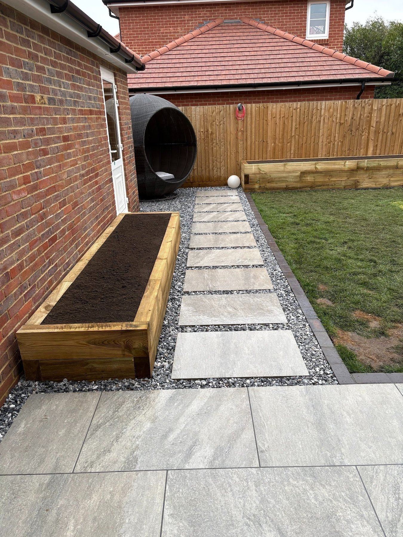 Stepping-stone path of sandstone in granite chippings, sleeper raised bed, porcelain terrace foreground — Warsash garden composition