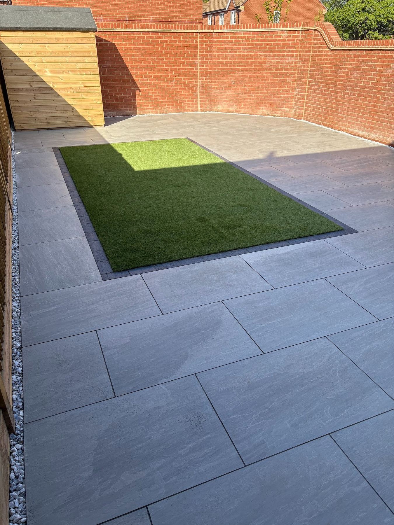The full hardscape composition with the lighter and darker porcelain zones meeting at the brick frame.