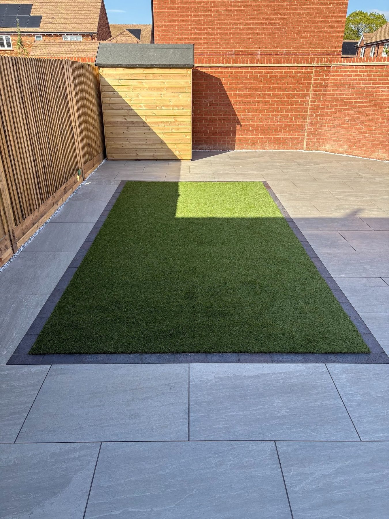 Two-zone porcelain garden — lighter textured porcelain across the foreground, darker large-format porcelain at the rear with a framed Astro turf insert bordered in solid blue engineering brick, Warsash
