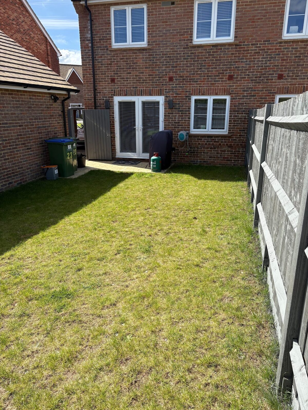 Before: the raw new-build rear plot with thin developer turf and a bare fence line.