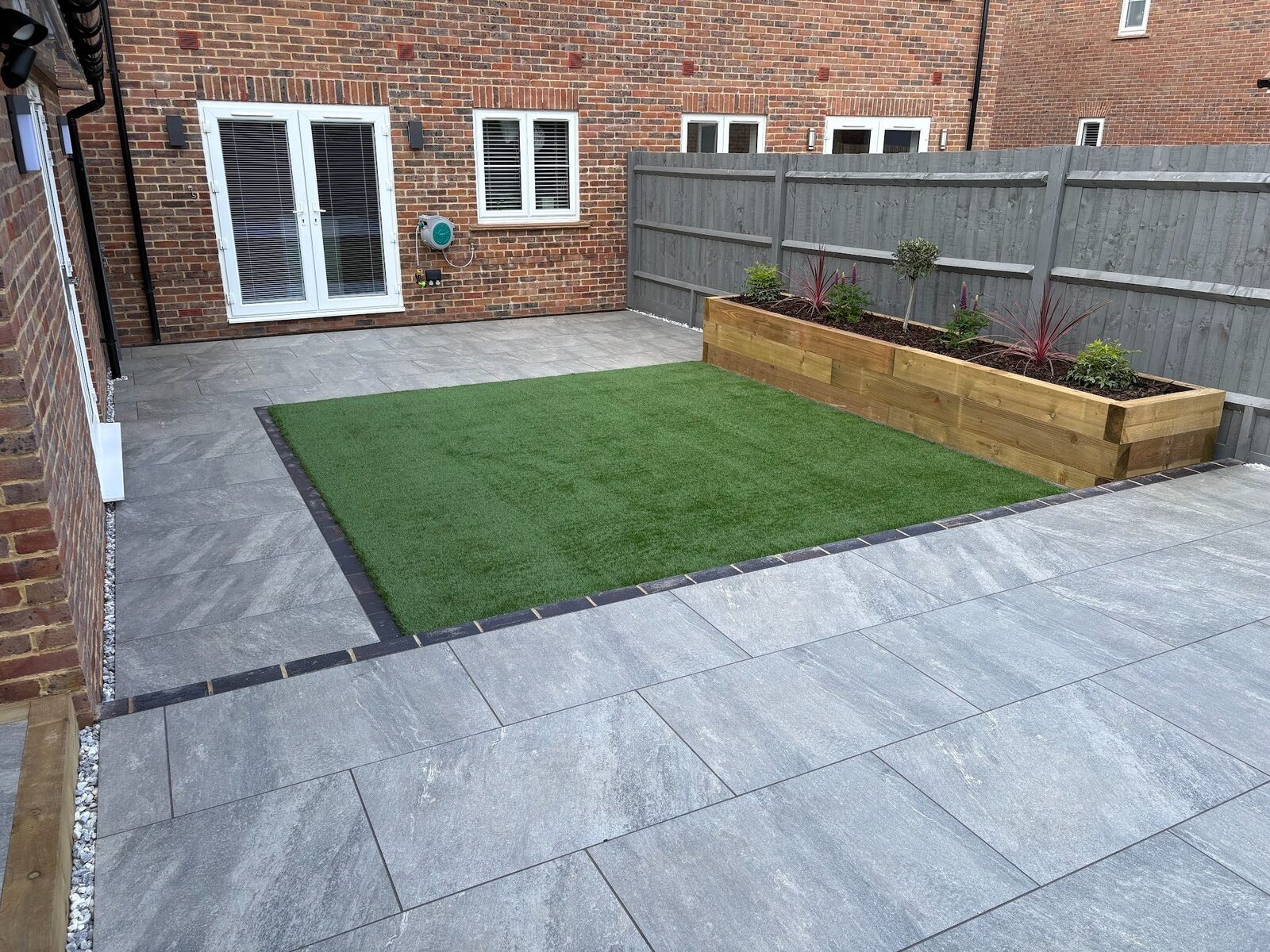 The artificial lawn set flush in large-format porcelain, framed on every side by a darker charcoal border course.