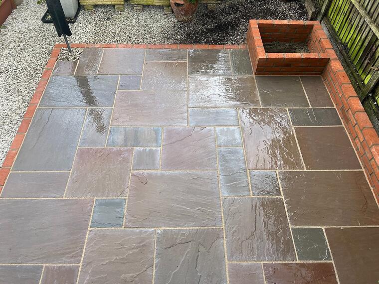 Bottom-of-garden patio, Fareham -- After rain — the sandstone tones come alive with moisture, showing the variation in slab colour the random course delivers.