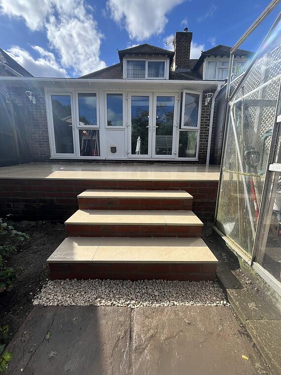 Decking to porcelain, Fareham -- A raised beige porcelain patio with matching brick-faced steps down to the lower garden, replacing the old timber decking.