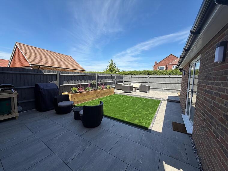 New-build garden, Warsash -- Large-format grey porcelain wrapping a central artificial lawn, an oak sleeper raised bed and rattan seating.