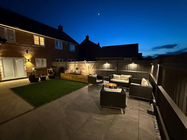 New-build garden, Warsash -- The rear terrace at dusk, lit for the evening with the seating area and framed lawn in view.